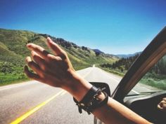 a person is driving down the road with their hand on the steering wheel, and there are hills in the background