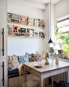 a room with a table, couches and shelves on the wall above it in front of a window