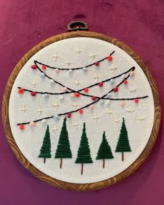 a hand embroidered christmas ornament hanging on a wall with string lights and trees