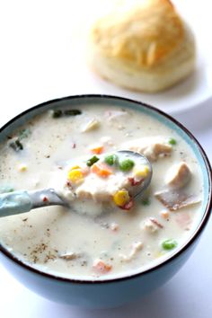 a bowl of soup with a spoon in it next to a biscuit on the table