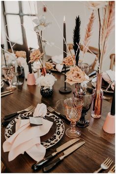 the table is set with black and white plates, silverware, pink napkins and flowers