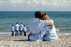 two people sitting on the beach with their backs to each other