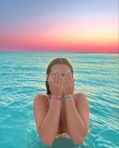 a woman covers her face while floating in the ocean at sunset with both hands over her eyes