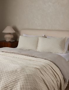 a bed with white sheets and pillows in a bedroom next to a lamp on a night stand