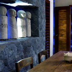 a wooden table sitting in front of a stone wall filled with vases and bottles