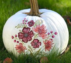 a painted pumpkin sitting in the grass with flowers on it's front and side