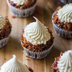 several cupcakes with white frosting and crumbled toppings on a wooden table