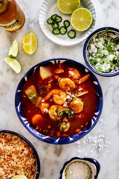 several bowls of food on a table with limes and other ingredients around them,