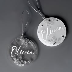 two personalized christmas ornament hanging from a string on a gray background with stars and snowflakes