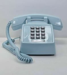 an old style telephone sitting on top of a white table next to a phone cord