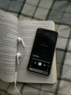 an open book with headphones laying on top of it next to a cell phone