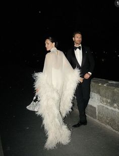 a man and woman dressed in formal wear walking down a street at night with one holding the other's hand