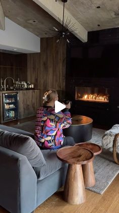 a woman sitting on a couch in front of a fire place and looking at the television