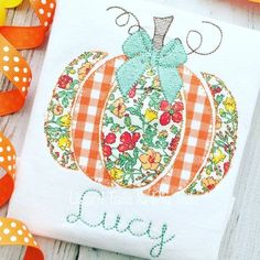 a pumpkin applique on a white t - shirt with orange and yellow ribbons