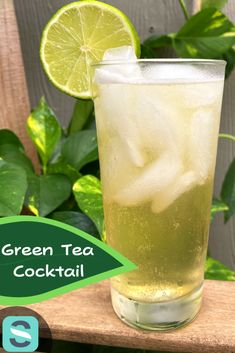 a tall glass filled with green tea and ice sits on a wooden table next to some leaves