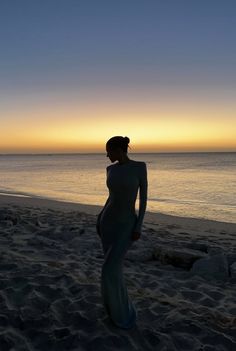 a woman standing on top of a sandy beach next to the ocean at sun set