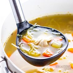 a ladle full of soup with chicken and carrots being held by a spoon