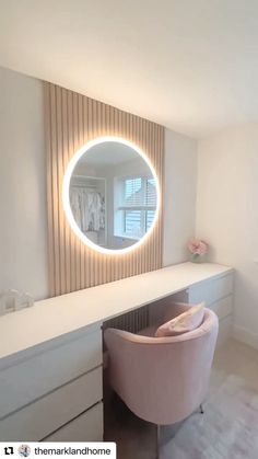 a round mirror on the wall above a dressing table with a pink chair in front of it