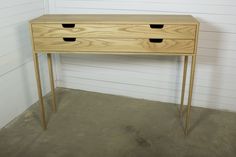 a wooden table with two drawers on it in front of a white wall and concrete floor