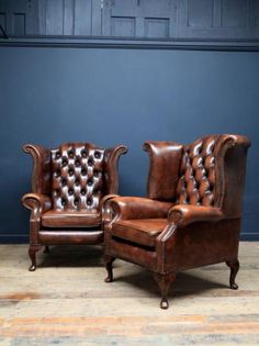 two brown leather chairs sitting next to each other on a wooden floor in front of a blue wall