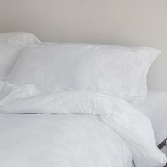 a bed with white sheets and pillows on top of it, next to a night stand