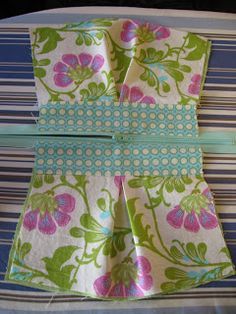 two pieces of fabric folded together on top of a striped table cloth with blue and green stripes