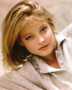 a woman with blonde hair and blue eyes posing for a photo in front of a wall