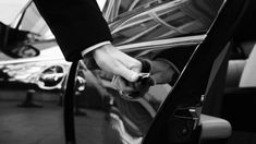 a person in a suit opening the door of a car with his hand on the keys