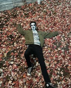 a person laying on the ground covered in leaves with their arms up and head painted like a skeleton