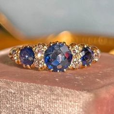 three stone ring sitting on top of a piece of gold foil with blue and white stones