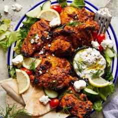 a blue and white plate topped with chicken, cucumber, tomatoes, lettuce and feta cheese