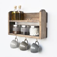 a wooden shelf with three mugs hanging from it's sides and spices on the hooks