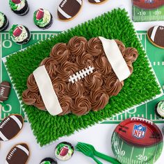 a football shaped cake sitting on top of a green field covered in cupcakes