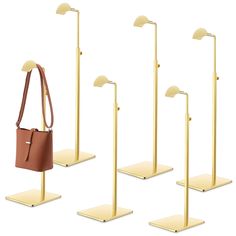 four gold - plated metal stands with brown leather bags on them, one holding a purse and the other carrying a tote bag