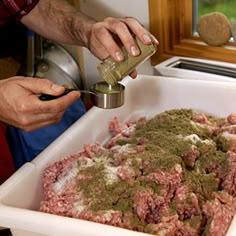 a person pouring something into a container filled with ground meat and seasoning in it