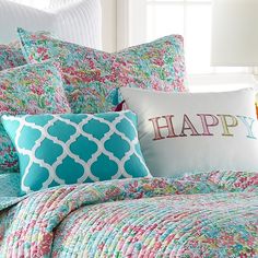 a bed with colorful pillows on it and a pillow that says happy in large letters