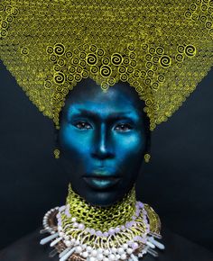 a woman with blue makeup and gold jewelry on her head is shown in front of a black background