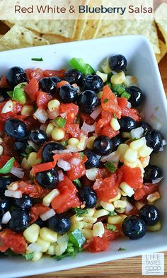 a white bowl filled with black olives, corn and tomato salsa next to tortilla chips