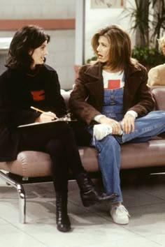 two women sitting on a couch talking to each other in front of a man holding a clipboard