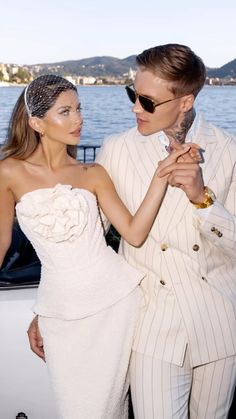 a man and woman standing next to each other in front of a boat on the water