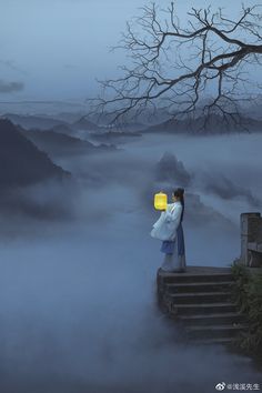 a woman standing on top of a mountain holding a yellow lantern