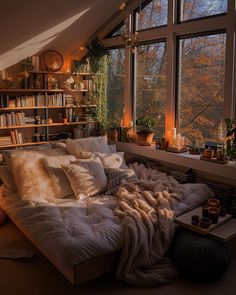 a bed with pillows and blankets on it in front of a window filled with books