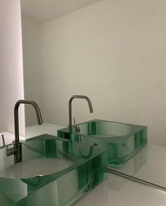 two green glass sinks sitting next to each other on top of a white countertop