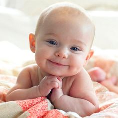 a smiling baby laying on top of a bed