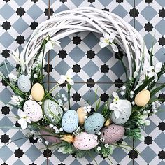 an easter wreath with eggs and flowers on a tiled floor in front of a black and white checkered wall