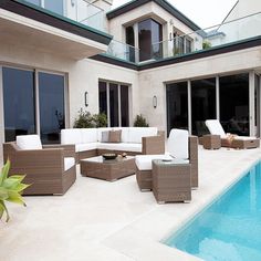 an outdoor living area with couches and tables next to a swimming pool in front of a house