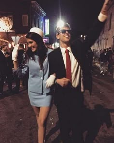 a man and woman walking down the street at night with their arms in the air