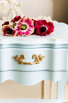 some flowers are sitting on top of a white table with gold trimmings and an ornate handle