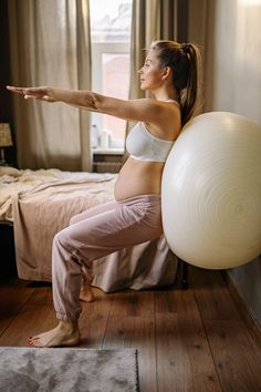 a pregnant woman is doing yoga with an exercise ball in her hand while sitting on the bed