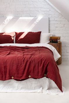 a bed with red sheets and pillows in a white room next to a brick wall